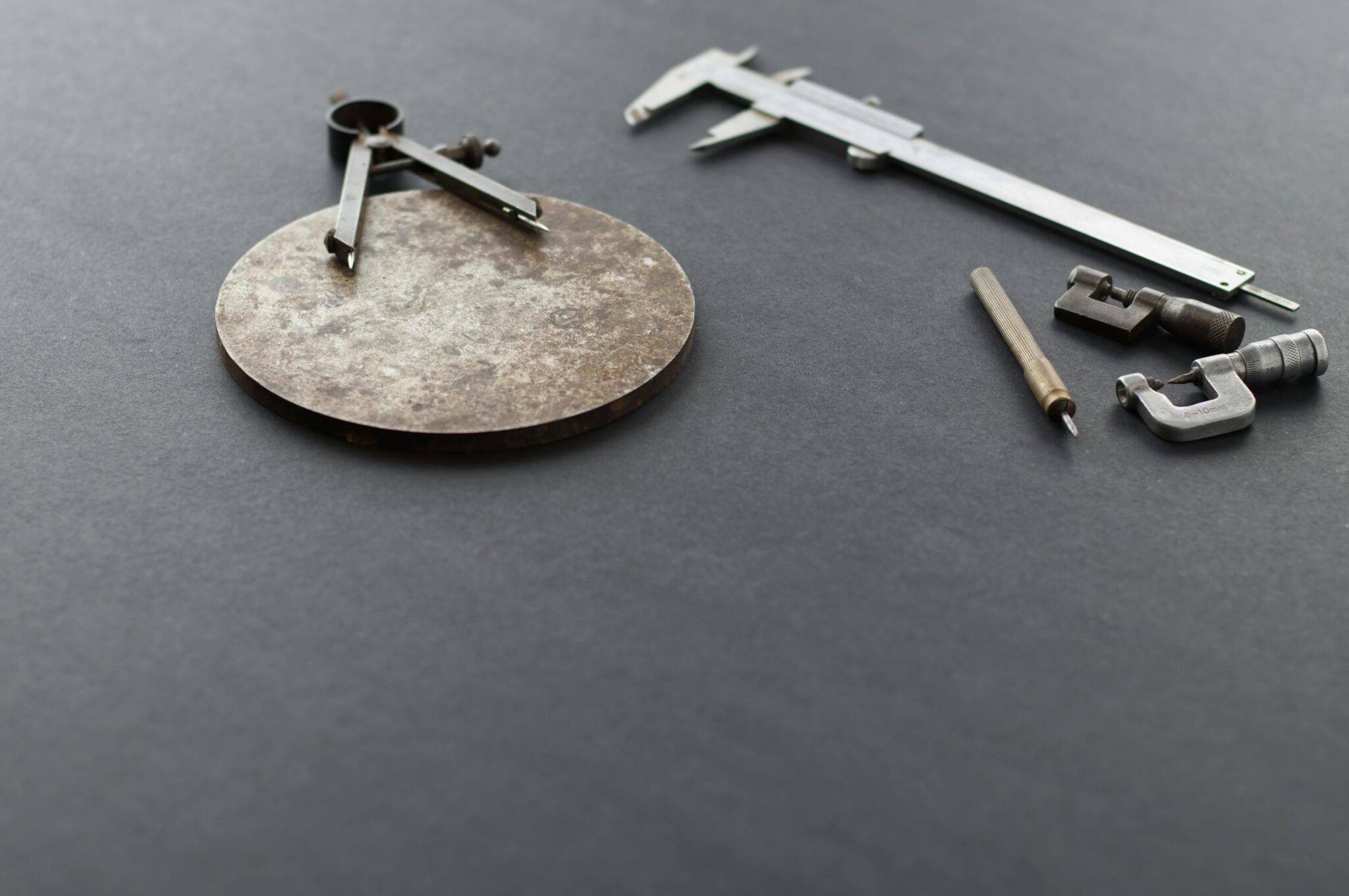 A selection of precision measuring tools, including calipers and a compass, on a black surface.